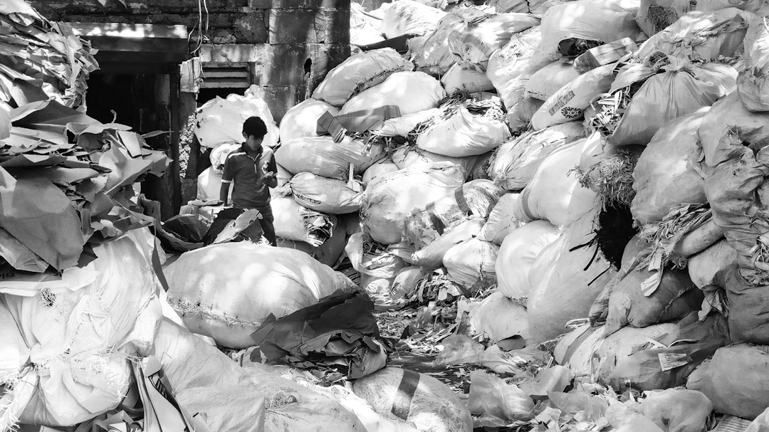 grayscale photo of man standing beside file of sack | The National Recycling Corporation